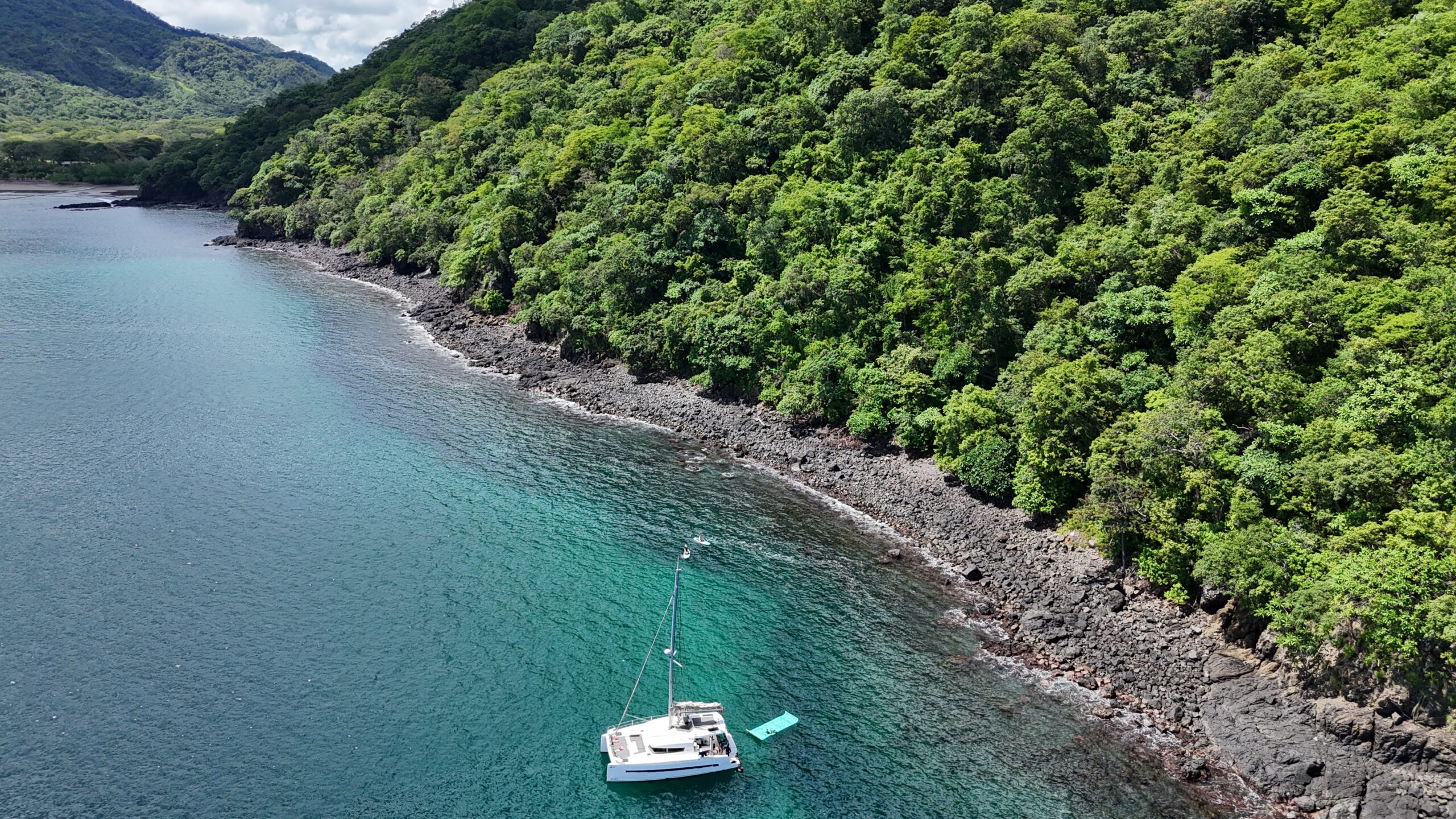 Sailboat anchored near lush coastline.